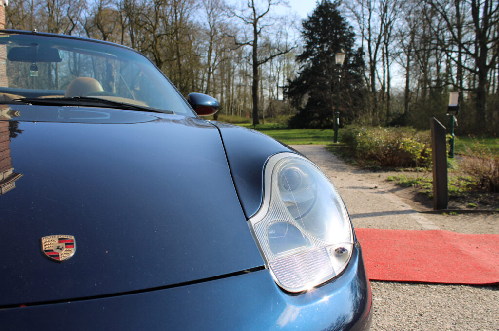 Blauwe Porsche 911 cabriolet geparkeerd op een grindpad met rode loper bij een landgoed